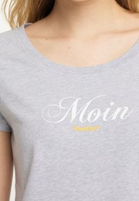 Gray cotton t-shirt with a scoop neckline, featuring the word "Moin" in white cursive font and a smaller gold text below it.