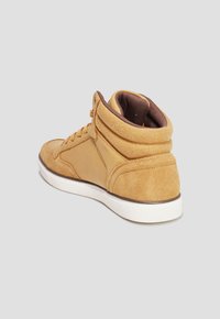 Zapatilla alta de tonalidad marrón, hecha de ante, con un collar acolchado, suela blanca de goma y forro de malla marrón. Presenta detalles de costura mínimos.