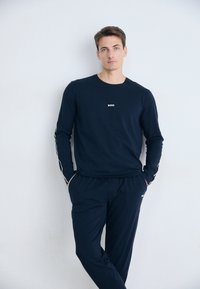 Námornícky modrý top s dlhým rukávom a zodpovedajúce nohavice s voľným strihom. Top má malé biele logo "BOSS"; nohavice majú bočné vrecká.