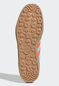 Adidas sneaker sole in tan with circular grip patterns; features a logo at center and textured accents for traction.
