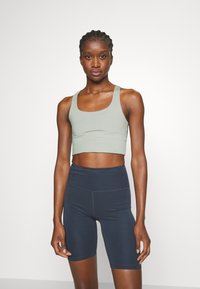 Svijetlozeleni crop top s širokim trakama i prilagođenim oblikom, uparen s visokim tamnoplavim šortsevima, oba izrađena od rastezljivog materijala.