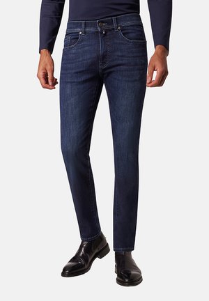 Donkere denim jeans met een slanke pasvorm, voorzien van een traditioneel ontwerp met vijf zakken en subtiele slijtagepatronen. Draagt zwarte leren laarzen.