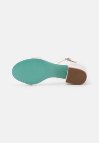 Sandal con tacco con una tomaia bianca texture, accenti argento e una suola in gomma turchese. Presenta una fascia decorativa con una fibbia regolabile.