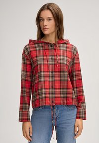 Giacca a quadri rossa con cappuccio, dettagli neri e beige, con chiusura a bottoni, vita regolabile con coulisse e maniche lunghe. Tessuto morbido.