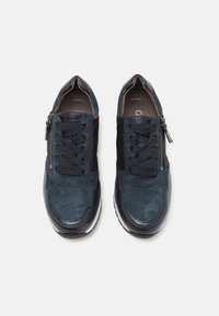 Sneakers in suede blu navy con un accento in pelle liscia; presentano una chiusura con lacci frontale e una cerniera laterale per una facile vestibilità; texture morbida e forma arrotondata.