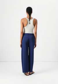 Brede marineblauwe broek met een ceintuur in de taille, gecombineerd met een aansluitend wit tanktop. Glad stoffen textuur, met zakken aan de achterkant.