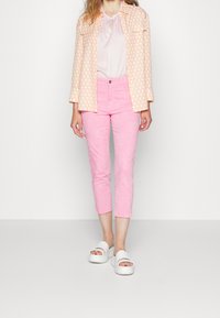 Chaqueta con estampado de melocotón, blusa rosa claro, pantalones rosados hasta el tobillo con textura floral y sandalias blancas gruesas. Diseño minimalista.