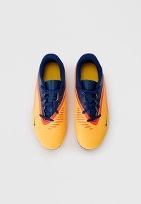 Des chaussures de soccer jaunes et marine avec un dessus texturé, présentant des accents rouges, une forme étroite et un logo noir. Les lacets sont d'un bleu foncé.