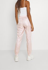 Rosa, glänsande, lätta joggerbyxor med elastisk midja och avsmalnande anklar, tillsammans med vita sneakers.