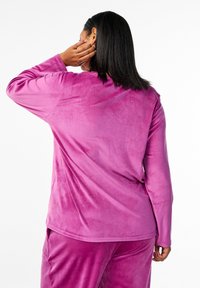 Set loungewear in velluto morbido fuchsia, composto da una maglia a maniche lunghe e pantaloni coordinati, con una texture liscia e una vestibilità comoda.