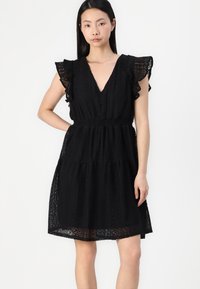 Vestido preto com decote em V, mangas curtas com babados e cintura elástica. O tecido tem um padrão texturizado com camadas em degraus.