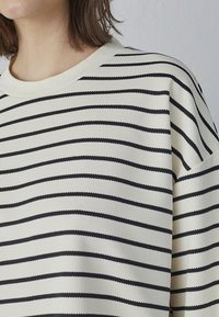 Stribet sweater i creme og sort med vandrette linjer, ribbet tekstur og rund halsudskæring. Stoffet fremstår blødt og let.