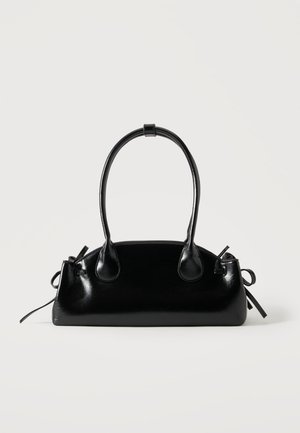 Petit sac à main noir brillant avec deux longues anses et des détails à cordon sur les côtés sur un fond clair uni.