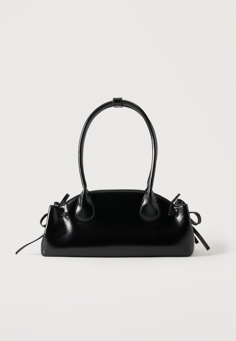 Petit sac à main noir brillant avec deux longues anses et des détails à cordon sur les côtés sur un fond clair uni.