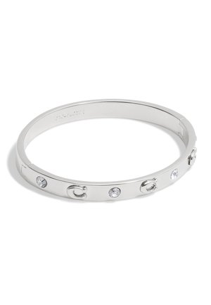 Silver metal bangle with a smooth surface, featuring clear crystals and a logo accent. The design is circular and sleek with a minimalistic style.