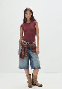 Bordo uska majica u kombinaciji s oversized trapericama do koljena, naglašena šarenim tkanim šalom i smeškim čizmama do gležnja.