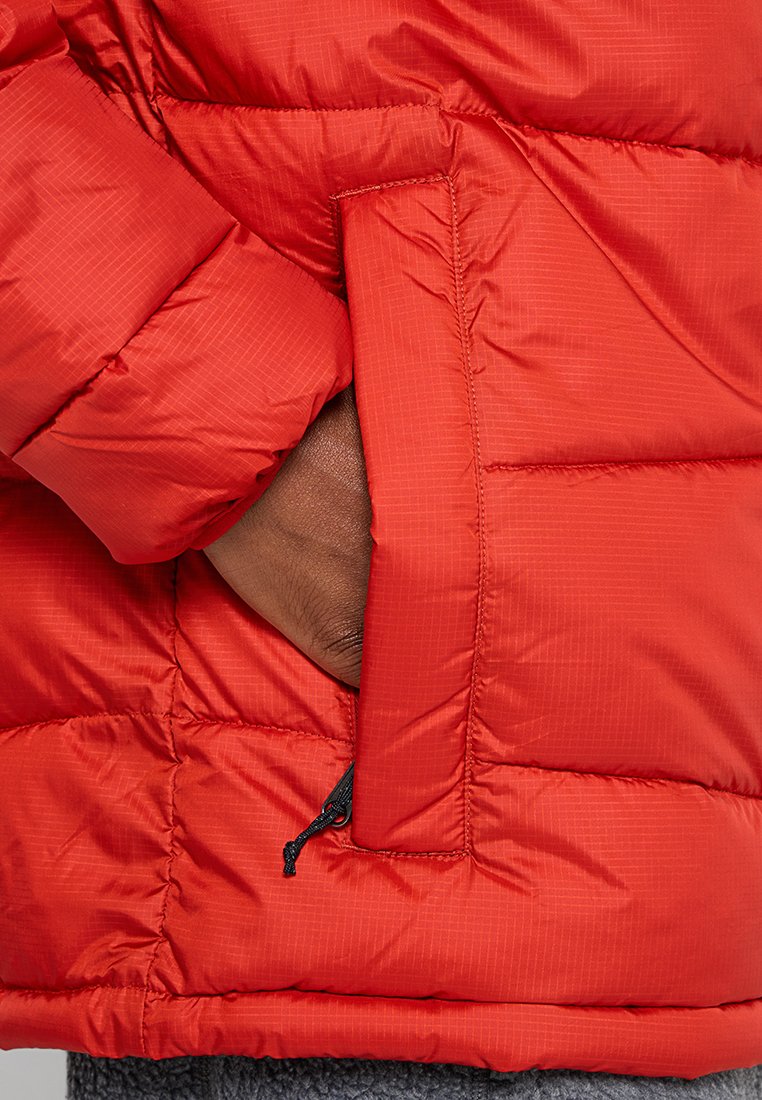 Chaqueta acolchada roja con un diseño de rombos. Cuenta con bolsillos laterales, una superficie texturizada y un cordón ajustable en el dobladillo.