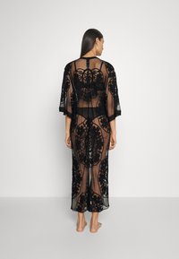 Czarny koronkowy kimono z haftem kwiatowym, z otwartym tyłem, rękawami do łokci oraz przezroczystą, lekką teksturą. Długi, zwiewny fason.