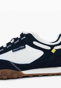 Adidași bleumarin și albi din suede și plasă, cu un etichetă care citește "De atunci 1984", având o talpă din cauciuc texturat de culoare maro și cusături contrastante.