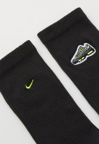 Μαύρες ριμπ κάλτσες με πράσινο κεντημένο λογότυπο Nike και σχέδιο παπουτσιού με νέον λεπτομέρειες στα πλάγια.