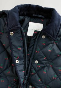Marineblau gesteppte Jacke mit kleinen Kirschmustern, Cordkragen, Metall-Druckknöpfen und einem Reißverschluss. Etikett innen sichtbar.