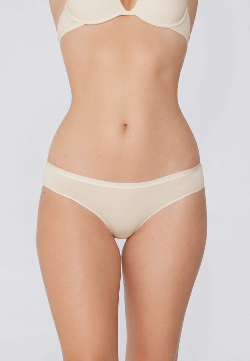 Slip in cotone beige con una texture liscia, dotati di una comoda vita ampia e cuciture minime per una vestibilità discreta.