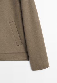 Mouw van een olijfgroene wollen jas met een gladde textuur, voorzien van een zijzak en nette, rechte randen.