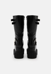 Black knee-high boots made of synthetic material, featuring two back zippers, adjustable straps, and a thick, textured platform sole.