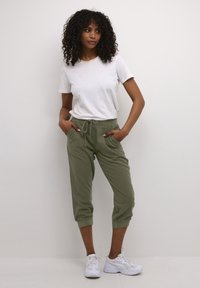 Lätt vit t-shirt kombinerad med olivgröna korta joggers med elastiska muddar och dragsko i midjan, tillsammans med vita sneakers.