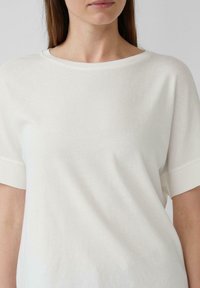 Witte top met korte mouwen en een ronde halslijn, gemaakt van een zachte, gladde stof. Het ontwerp heeft een ontspannen pasvorm en een minimalistische stijl.