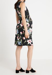 Vestido negro con estampado floral, con un corsé ajustado, diseño sin mangas y falda hasta la rodilla con flores rosas y azules, combinado con mules negros.
