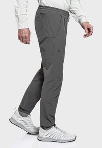 Graue leichte Hose mit elastischem Bund, seitlichen Taschen und dezentem Logo-Detail. Getragen mit weißen Sportschuhen und grauen Socken.