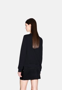 Sudadera negra de mangas largas, con tejido texturizado y cuello redondo, combinada con una falda corta negra que presenta brillantes acentos de lentejuelas.