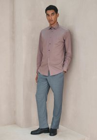 Męska koszula z długim rękawem zapinana na guziki w kolorze mauve z kołnierzem typu spread, zestawiona z jasnoszarymi dopasowanymi spodniami i czarnymi eleganckimi butami.