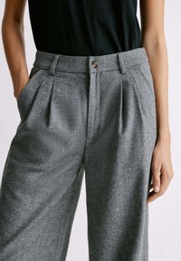 Pantalones de espiga grises con un ajuste relajado, que cuentan con bolsillos laterales, pinzas y una cinturilla con cierre de botón. Fabricados con un tejido texturizado.