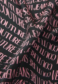 Fekete anyag, rajta ismétlődő rózsaszín szöveggel, a "COUTURE" és "JEANS" szavakkal különböző tájolásokban és méretekben. Puha textúra.