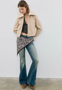 Beige zip-up bunda s límcem z umělé ovčí vlny, olivová tílko, rozšířené modré džíny a hnědý bandana se zebrovým potiskem. Hnědé lodičky na šněrování.