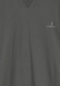 Camiseta de cuello en V de color gris oscuro hecha de una tela suave con una textura sutil. Cuenta con un pequeño logo impreso en el lado izquierdo.