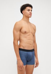 Męskie niebieskie szorty z miękkiego materiału, z czarnym elastycznym pasem w brandingiem. Krój dopasowany, podkreślający sylwetkę.