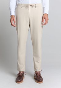 Beige broek van gladde stof, met een elastische tailleband en koord, taps toelopende pasvorm, gecombineerd met bruine schoenen met contrastveters.