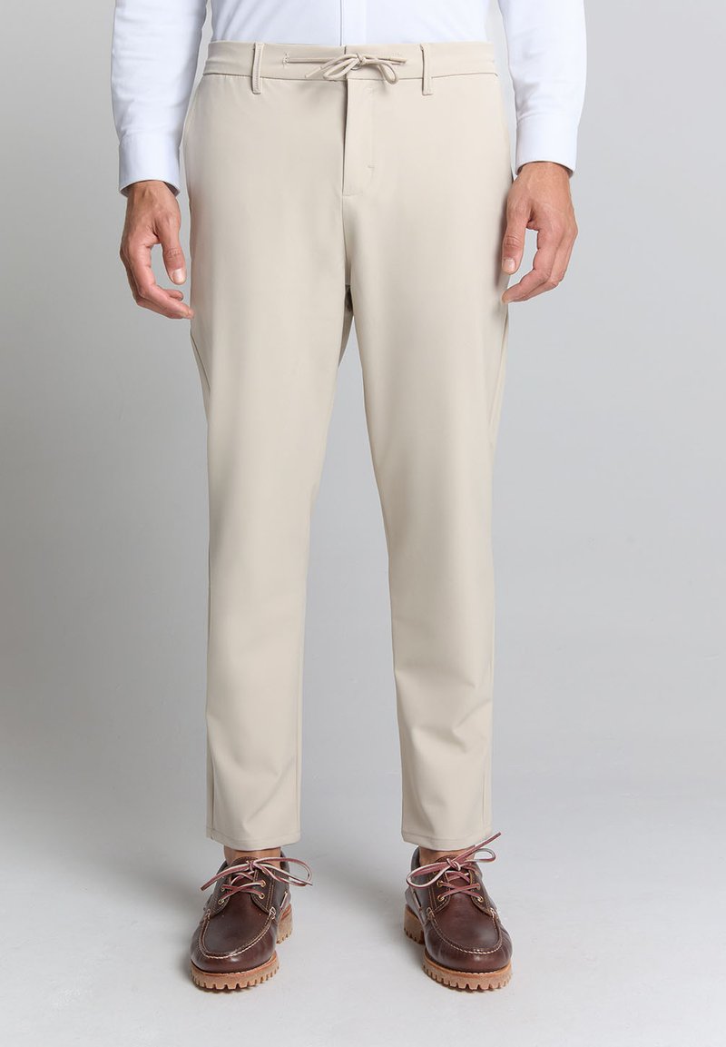 Beige broek van gladde stof, met een elastische tailleband en koord, taps toelopende pasvorm, gecombineerd met bruine schoenen met contrastveters.