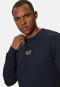 Felpa blu navy realizzata in tessuto morbido, con maniche lunghe e colletto a girocollo. Presenta un piccolo logo bianco sul petto.