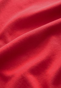 Tessuto di cotone rosso con una texture liscia, caratterizzato da pieghe e grinze delicate, che indicano morbidezza e una caduta flessibile.
