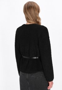 Zwarte gebreide trui met een ontspannen pasvorm, voorzien van een ronde halslijn en lange mouwen, strakker gemaakt in de taille met een zwarte riem.