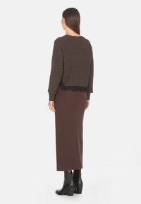 Maglione marrone a coste con bordo in pizzo nero all'orlo, abbinato a una gonna marrone aderente e stivaletti neri con tacco.