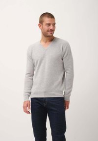 Suéter gris de punto acanalado con escote en V, mangas largas y un diseño ajustado, combinado con jeans de mezclilla oscuros. Textura suave y estilo minimalista.