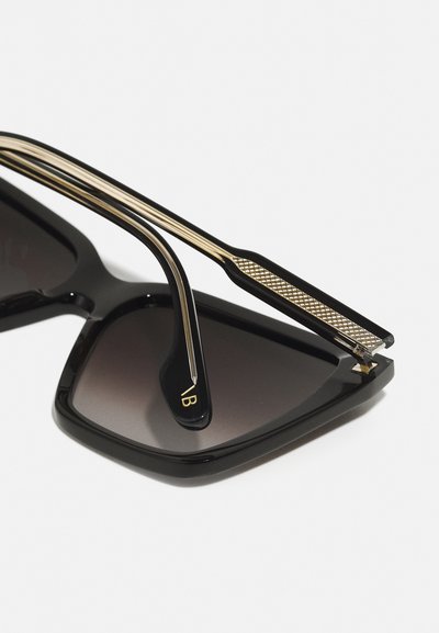 Black square sunglasses with gradient dark lenses, featuring gold accents and textured metal detail on the arm, sleek and modern design.