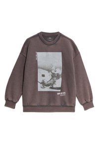 Felpa oversized marrone in cotone, con stampa grafica di uno skateboarder in bianco e nero. Polsini e scollatura a coste.