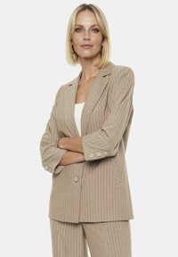 Beżowa marynarka w prążki z klapami, podwójnymi guzikami i rękawami o długości trzech kwart. Wykonana z teksturowanej tkaniny, dopasowany krój.