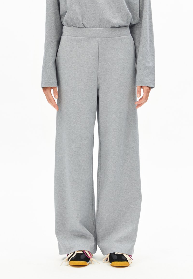 Grauweite Hosen aus weichem Stoff mit glatter Textur und einem elastischen Bund, getragen mit schwarzen Turnschuhen mit mehrfarbigen Akzenten.